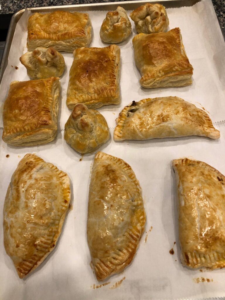 empanadas of all sizes and different crusts on a baking sheet